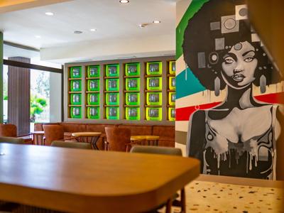 Moderne hotel lounge met kleurrijke kunstwerken, houten tafels, leren stoelen en grote ramen.