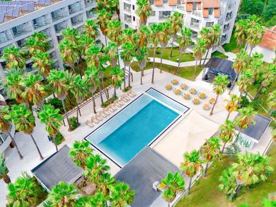 Hotel complex with large rectangular pool surrounded by palm trees and lounge chairs.