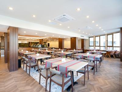 Ruime hotel eetzaal met moderne tafels, stoelen en grote ramen die natuurlijk licht binnenlaten.