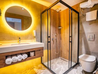 Moderne hotelbadkamer met verlichte spiegel, glazen douche en aanrecht met opgerolde handdoeken.