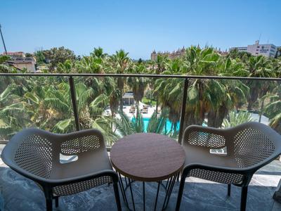 Balkon met twee stoelen en tafel met uitzicht op palmbomen en een zwembad.