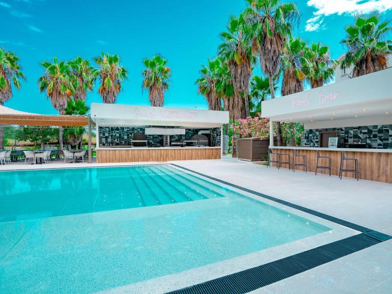 Helder zwembad omringd door palmbomen en witte poolbars onder een blauwe lucht.