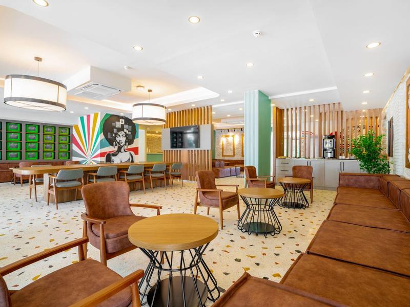 Ruime hotellounge met moderne zitplaatsen, groene accenten en artistieke wanddecoratie.