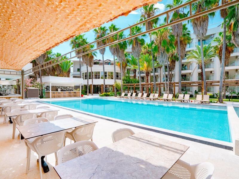 Buitenzwembad met witte tafels, stoelen, palmbomen en hotel op de achtergrond.