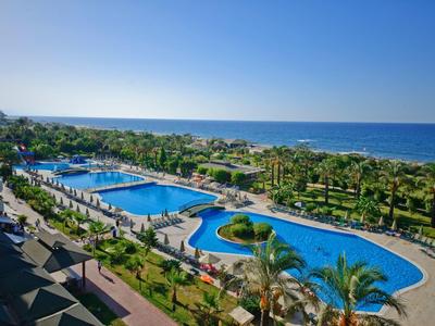 Resort pool area with palm trees and ocean view under clear sky.