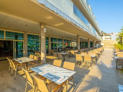 Outdoor hotel dining area with tables and chairs under a covered walkway in sunny weather.