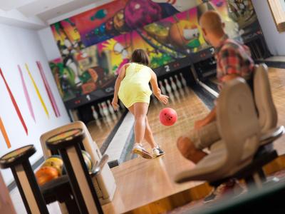 Dos personas juegan a los bolos en una bolera decorada con colores vivos.