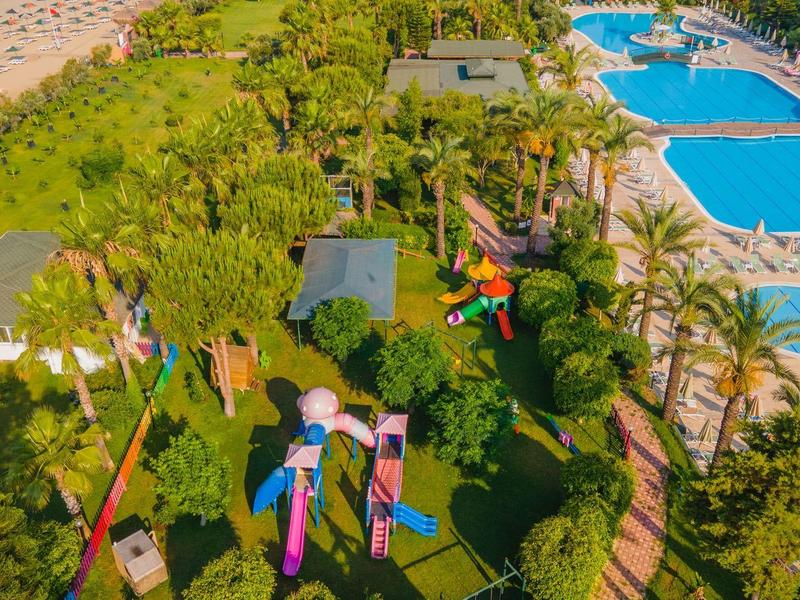 Beachside resort with pools, palm trees, and colorful lounge chairs on green lawn.