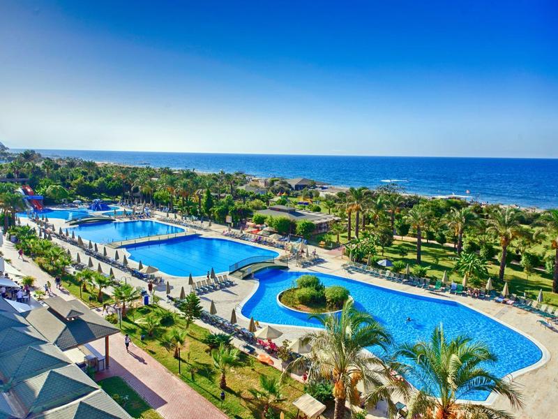 Resort with two large swimming pools, palm trees, and a view of the sea under a clear sky.
