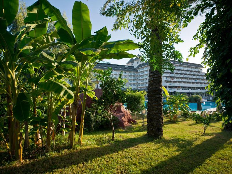 Resort building viewed through lush tropical plants and palm trees on a sunny day.
