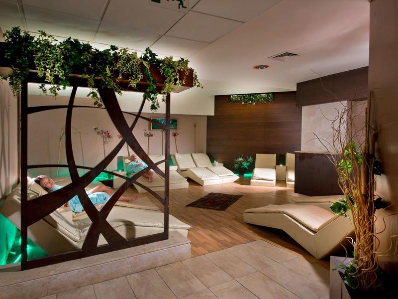 Cozy hotel spa room with loungers, soft lighting, plants, and a wooden wall feature.