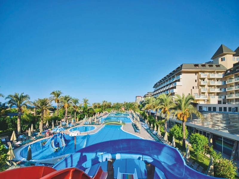 Outdoor pool area with palm trees and lounge chairs at a resort under a clear sky.
