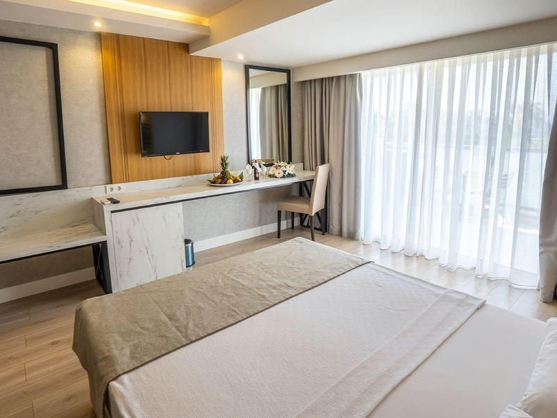 Hotel room with a bed, desk, TV, and large window with curtains.