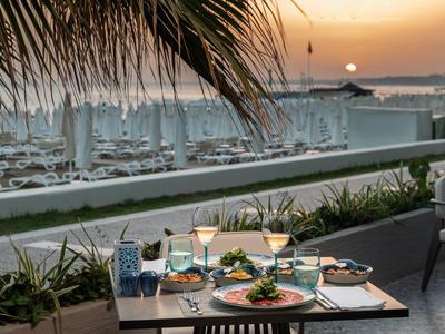 Abendessen auf Terrasse mit gedecktem Tisch, Palmen und Segelbooten im Hafen bei Sonnenuntergang.