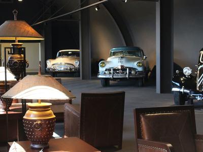 Intérieur d'un hôtel avec meubles en cuir et voitures vintage exposées en arrière-plan.