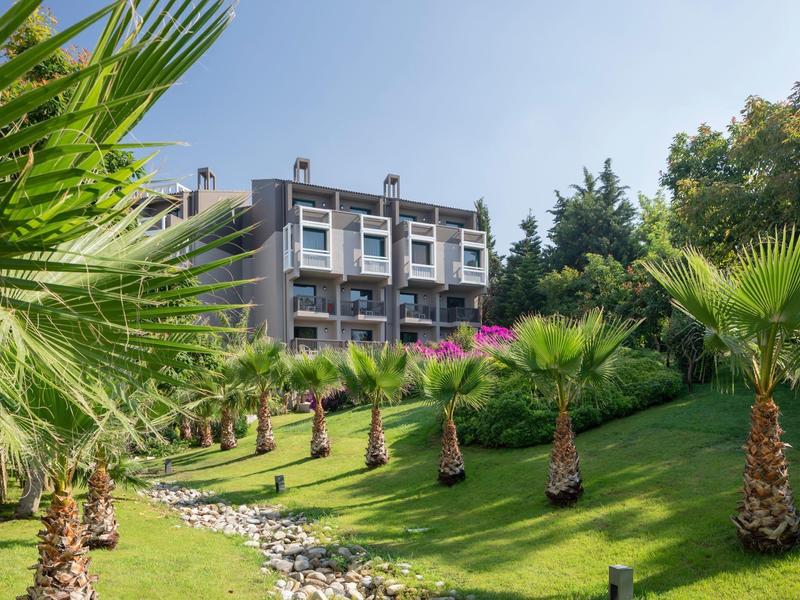 Hôtel moderne avec pelouse verdoyante et palmiers sous un ciel clair.
