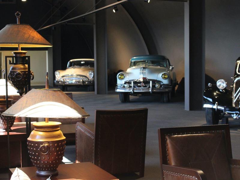 Intérieur d'un hôtel avec meubles en cuir et voitures vintage exposées en arrière-plan.