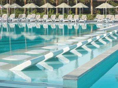 Hotelový bazén se zabudovanými sedadly ve vodě a lehátky s deštníky po stranách.