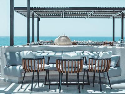 Moderní venkovní prostor s kulatou pohovkou, dřevěnými stoly a výhledem na moře.