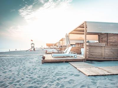 Plaża z drewnianymi leżakami i daszkiem, miękkie poranne słońce nad morzem.