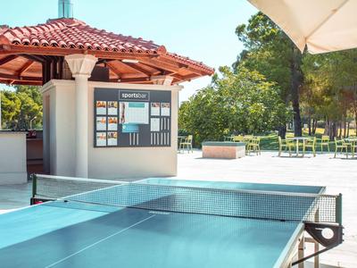 Stół do ping-ponga na zewnątrz hotelu z parasolem i kioskiem w tle.
