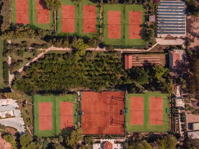 Letecký pohled na tenisové kurty obklopené stromy a budovami.