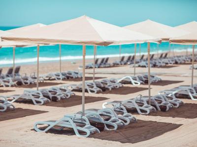 Řady bílých lehátek pod slunečníky na pláži s modrým mořem v pozadí