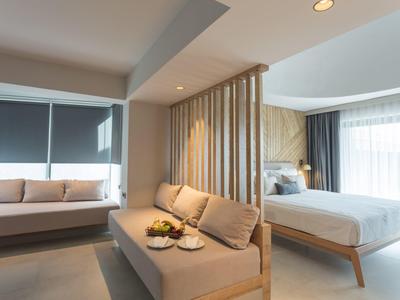 Světý hotelový pokoj s manželskou postelí, pohovkou a velkým oknem s závěsy.