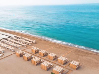 Prázdná písečná pláž s řadami lehátek a dřevěných chatek u klidného modrého moře.