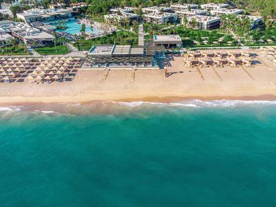Letecký pohled na resort s písečnou pláží, slunečníky a tyrkysovým mořem.