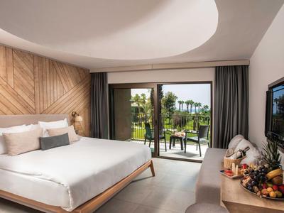 Nowoczesny pokój hotelowy z podwójnym łóżkiem, sofą, drzwiami na taras i widokiem na zielony ogród.