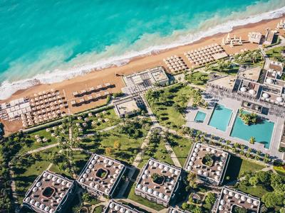 Letecký pohled na resort s pláží, několika bazény a zelenými zahradními oblastmi.
