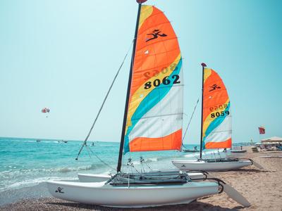 Dwa kolorowe katamarany z żaglami na plaży obok morza pod niebieskim niebem.