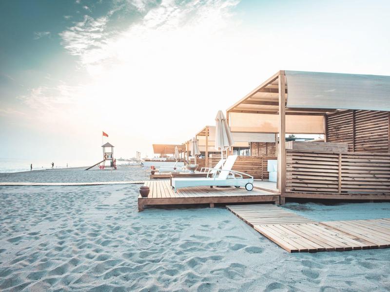 Pláž s lehátky a dřevěnými boudami při východu slunce u vody.