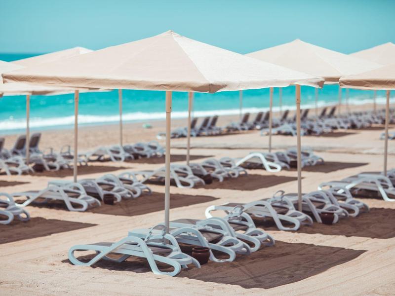 Řady bílých lehátek pod slunečníky na pláži s modrým mořem v pozadí