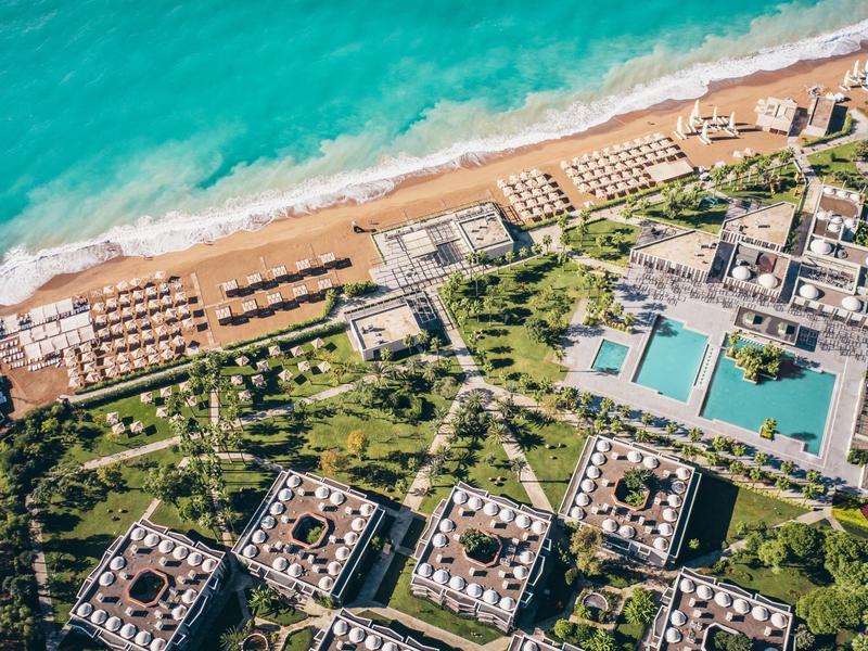 Letecký pohled na resort s pláží, několika bazény a zelenými zahradními oblastmi.