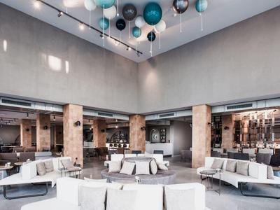 Großer heller Warteraum mit weißen Sofas, grauen Wänden und bunten Kugeln an der Decke.