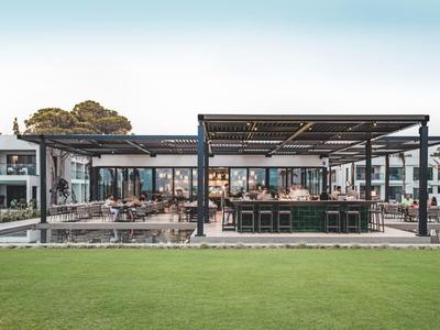 Modernes, offenes Restaurant mit großem Außensitzbereich, Holz- und Metallstruktur, grünem Rasen im Vordergrund.