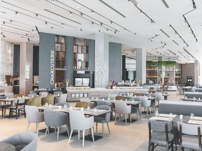 Moderne, helle Cafeteria mit vielen Tischen, grauen Stühlen und einer Kuchentheke im Hintergrund.