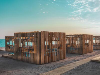 Strand mit mehreren quadratischen Holzhütten, blauer Himmel und ruhiges Meer im Hintergrund.