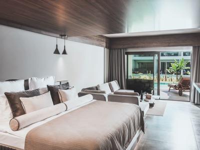 Modernes Schlafzimmer mit großem Bett, Holzwand, Sofa und Glasfront mit Blick auf Terrasse.