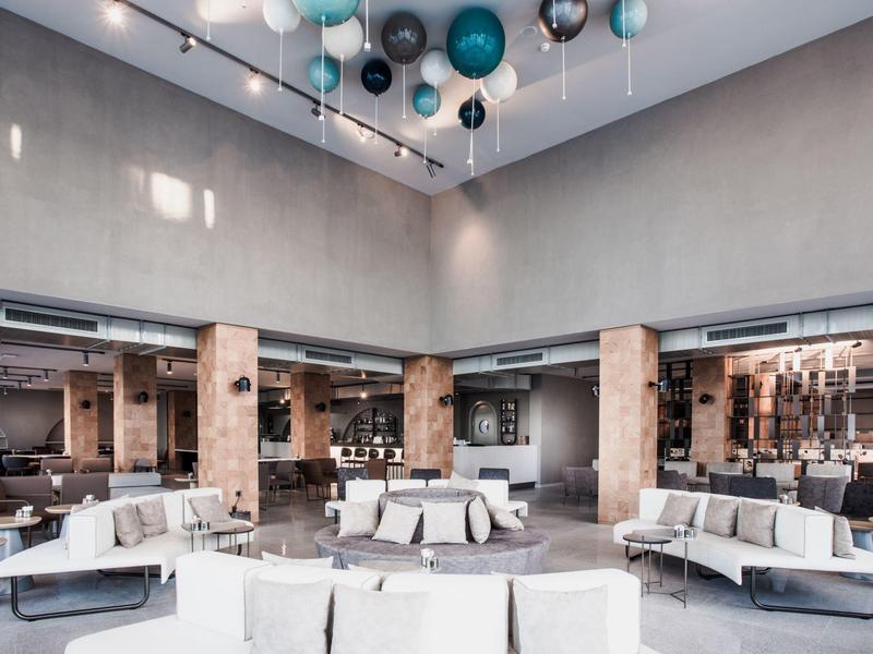 Großer heller Warteraum mit weißen Sofas, grauen Wänden und bunten Kugeln an der Decke.