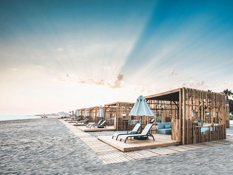 Strand mit Holzbungalows, Liegestuhl und Sonnenschirm bei Sonnenaufgang oder -untergang.