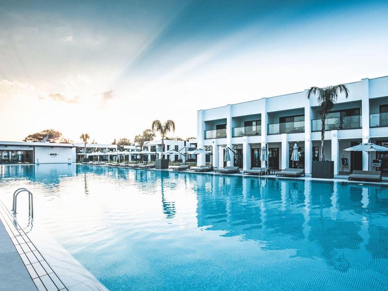 Großer Außenpool mit klar blauem Wasser und modernem weißem Gebäude im Hintergrund bei Sonnenuntergang.