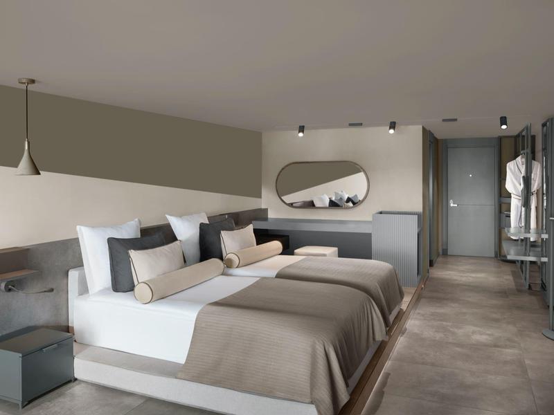 Modernes Hotelzimmer mit zwei Doppelbetten, grauen Wänden und minimalistischer Einrichtung.