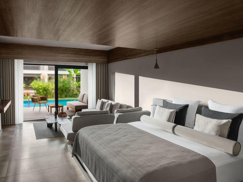 Modernes Hotelzimmer mit zwei Betten, Sofa, Fernseher und Zugang zu Terrasse mit Pool und Garten.