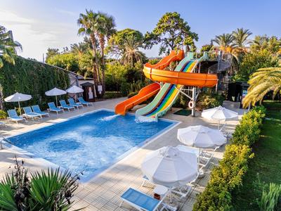 Außenpool mit bunten Wasserrutschen, weißen Schirmen und Palmen in sonniger Umgebung.
