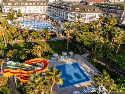 Große Hotelanlage mit Pool, Wasserrutsche, Palmen und weitläufigen Gartenanlagen bei Sonnenschein.