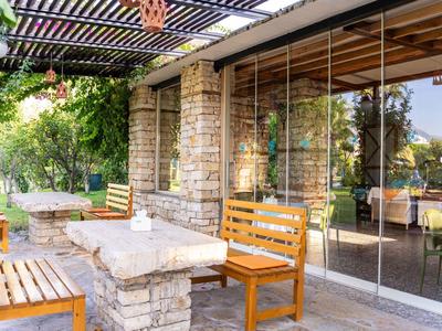 Gemütliche Terrasse mit Holzbank, Steintisch und Glaswand, umgeben von Grün und Licht.
