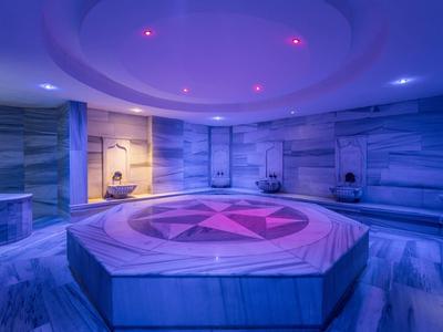 Moderner runder Hamam mit blauen Marmorwänden, zentralem achteckigem Tisch und violetter Beleuchtung.